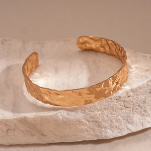 Golden wide open cuff bracelet with hammered texture on a natural stone background