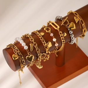 Golden OT buckle heart and pearl charm bracelets set displayed on a wooden jewelry stand