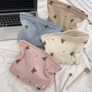 Corduroy makeup bags with bear pattern in pink, blue, and cream organized on a bed