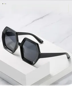 Detail of black geometric hexagonal sunglasses with thick frames on a marble background