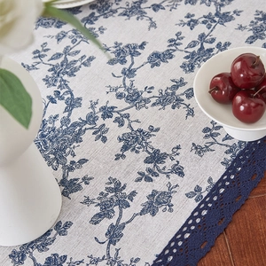 Detail of white cotton linen table runner with blue floral pattern and lace trim