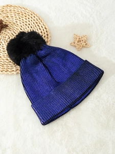 Close-up of metallic blue knit beanie with black pompom on a soft white background