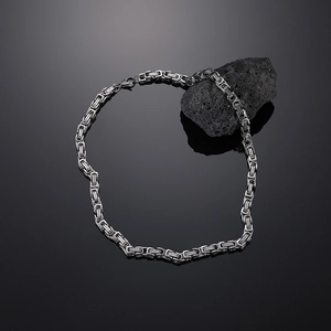 Close-up of silver Byzantine chain with lobster clasp on a textured black volcanic rock
