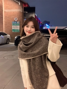 Close-up of a brown knit scarf with beige scalloped trim worn by a model at night