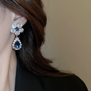 Detail of silver flower earrings with blue cubic zirconia teardrop pendants on a model