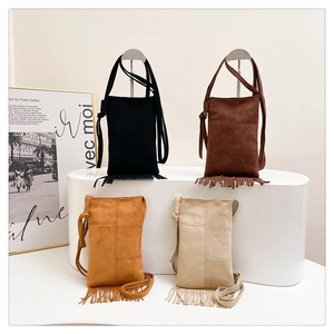 Detailed close-up of fringe crossbody bags in four colors on minimalist display stand