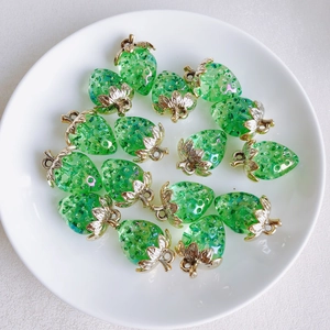 Close-up of green resin strawberry charms with gold leaves in a white ceramic dish