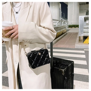 Detail of a black quilted PVC jelly bag with gold chain strap on a city street