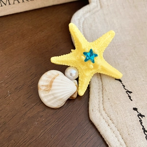 Detail of yellow starfish hair clip with blue crystal, white pearl and seashell texture
