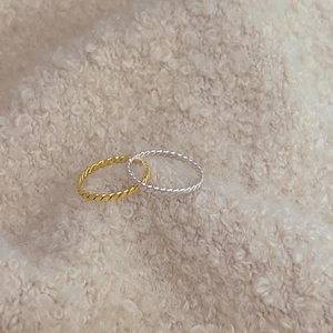 Macro detail of twisted silver and gold rings on a soft beige knit fabric background