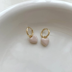 Gros plan de boucles d'oreilles créoles dorées avec pendentifs cœurs rose pâle