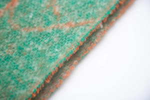 Macro view of green and orange boucle jacquard knit fabric showing fringe and texture