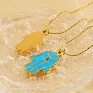 Macro detail of Hamsa Hand and Blue Evil Eye pendants on gold snake chain jewelry