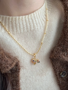 Detail of gold necklace with pearls and rainbow gemstone bow pendant worn by a model