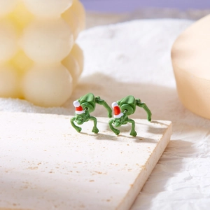 Close-up of funny green frog earrings wearing red Santa hats on a rustic stone display