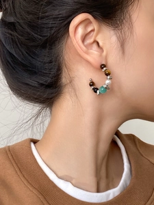 Detail of C-shaped earrings with tiger eye and opal beads on a female model