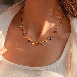 Detail of model wearing a gold sweater chain with vibrant multi-color gemstone pendants