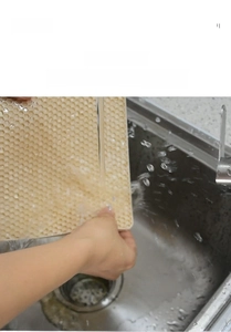 Washable light beige silicone honeycomb mat being rinsed under a water faucet
