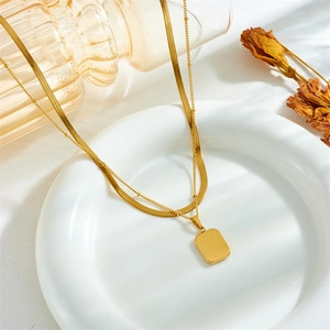 Close-up of double-layered gold necklace with rectangular pendant on a white ceramic dish