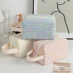 Detailed view of tweed cosmetic bags in blue, beige, and pink with woven texture