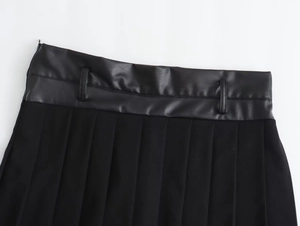 Detailed close-up of faux leather waistband and pleated fabric on black skirt shorts