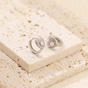 Macro shot of silver heart earrings with sunburst texture and center sparkling gemstone
