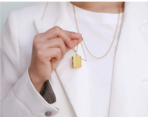 Detail of a golden book-shaped locket pendant held against a white blazer backdrop