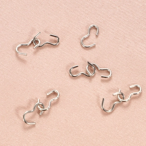 Detailed view of multiple silver stainless steel S-shaped jewelry clasps on pink fabric
