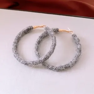 Grey wool knitted hoop earrings with gold metal clasp on minimalist beige background