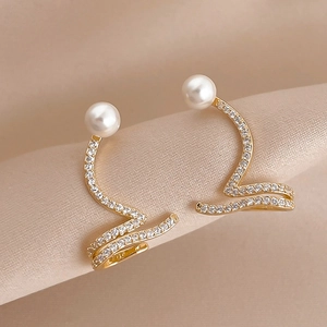 Close-up of elegant gold snake-shaped earring with white pearl and inlaid crystals
