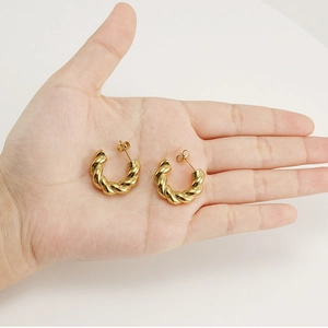 Close-up of golden twisted C-shaped earrings on hand showcasing metallic texture