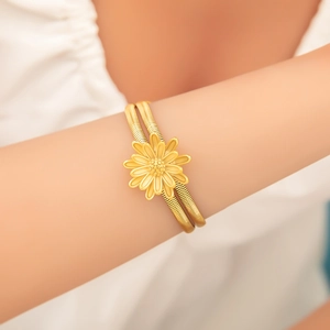 Detail eines goldenen zweilagigen Spiralarmbands mit zarter Gänseblümchenblüte am Handgelenk
