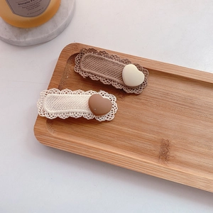 Detail view of two beige knitted BB hair clips with matte heart accents on wood