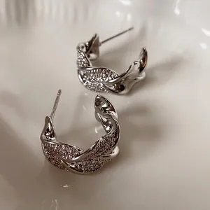 Elegant C-shaped twisted earrings with pavé cubic zirconia on a cream ceramic plate