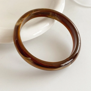 Detail view of a slim amber tortoiseshell resin bangle on a white ceramic plate