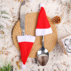 Mini Christmas hat cutlery holders in red and white fabric on snowy wooden background