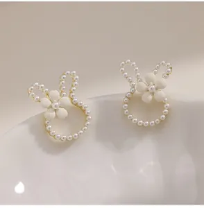 Close-up of rabbit-shaped pearl earrings with white flower detail on a ceramic bowl