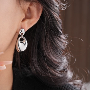 Close-up of minimalist irregular oval silver metal earrings worn by a model in bright light