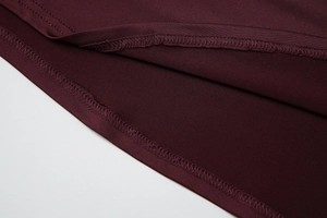 Détail de la couture surjetée haute densité et texture du tissu tricoté bordeaux sur la robe
