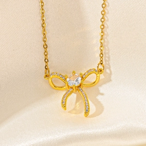 Macro shot of gold bow pendant with white cubic zirconia on silky white satin background