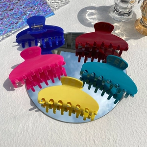 Five colorful large acetate hair claws on a mirror with a blue sky reflection