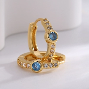 Golden hoop earrings with blue round zircon and white side stones on neutral background