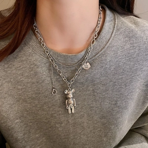 Detail of layered silver necklaces with Bearbrick style pendant and engraved disk on hoodie