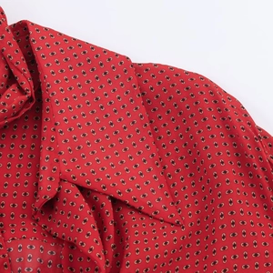 Vue détaillée du chemisier rouge avec motif chaîne géométrique noir et or et col à noeud