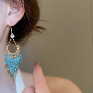 Detail of elegant gold tassel earrings with light blue crystals worn by a model