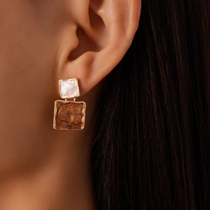 Close-up of geometric square earrings with white enamel and brown marble pattern