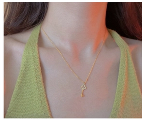 Detail of gold-plated silver key necklace with sparkling zircon clover pendant on neck