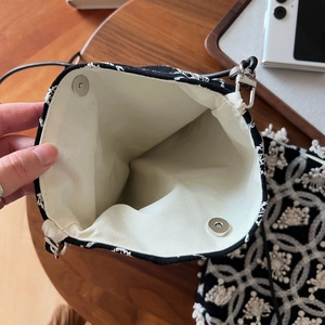 Detail of white embroidery pattern and magnetic metal snap closure on small canvas bag