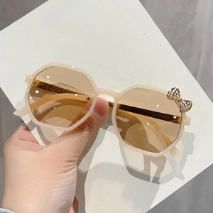 Detail of beige octagonal kids sunglasses with a golden metal bow on light brown lens