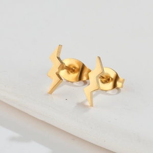Macro detail of minimalist gold lightning bolt stud earrings on marble texture surface